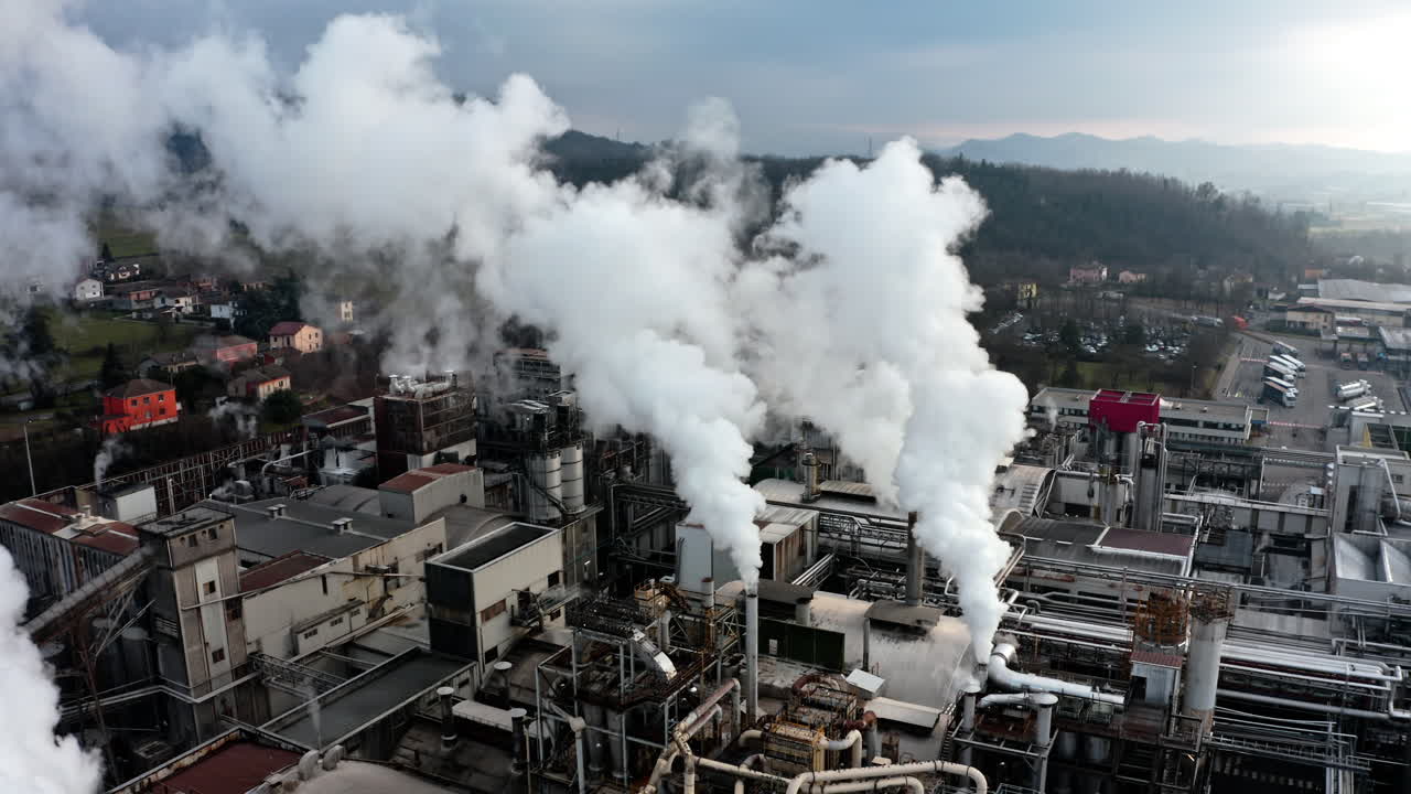Industrial factory emitting thick white smoke from multiple chimneys in a rural setting