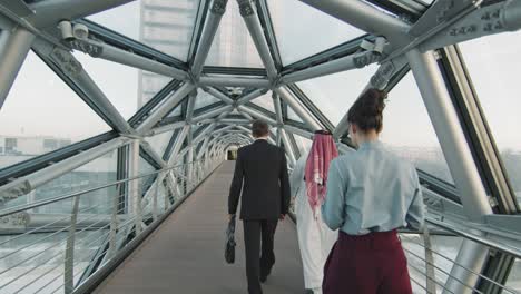 business people going to work along indoor glass bridge