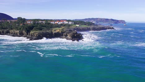 Aerial-landscape-view-of-the-coast-in-Cantabria,-Spain-with-the-town-in-the-background