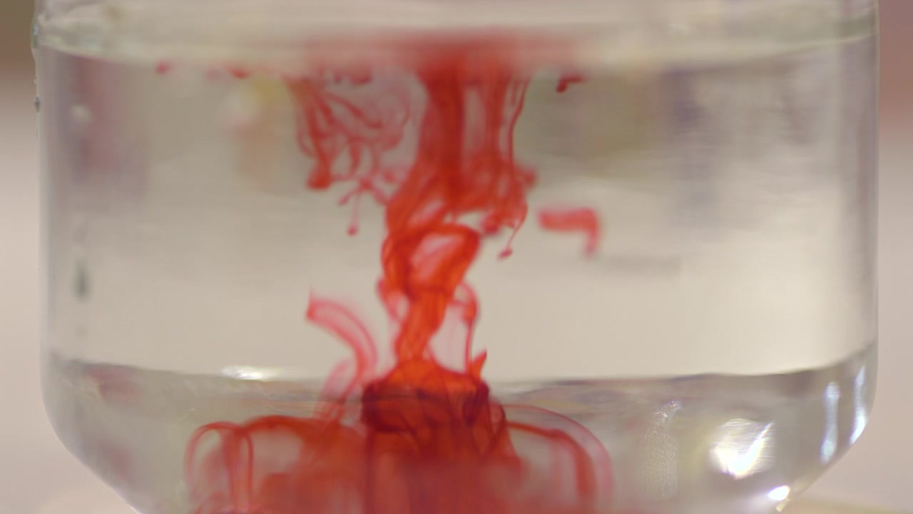 Primo piano di inchiostro rosso che si disperde nell'acqua limpida, creando forme astratte fluide e motivi organici. Ideale per la creatività, il movimento fluido e gli sfondi artistici.