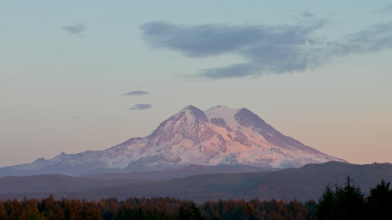 Ripresa aerea con drone del Monte Rainier che risplende al tramonto con luce soffusa sulla cima innevata e la foresta sottostante