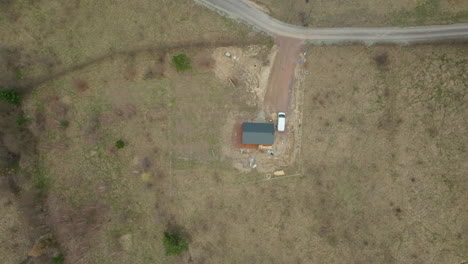 Perspectiva-Aérea-De-Una-Pequeña-Casa-En-Construcción-En-Una-Zona-Apartada,-Con-Una-Furgoneta-Blanca-Estacionada-Cerca