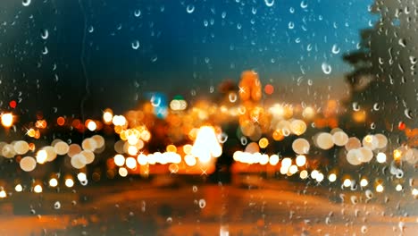 rain drops falling on glass window on urban background beautiful colorful bokeh light effect.