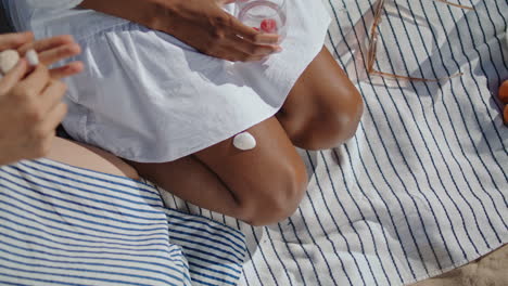 manos de primer plano ponen piedras en las piernas de la mujer picnic de verano. dos chicas lgbt divirtiéndose