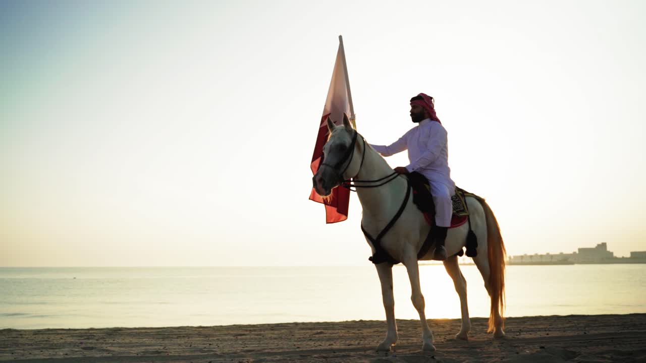 Un cavaliere a cavallo che tiene la bandiera del Qatar vicino al mare-5.