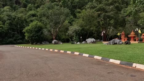 a tranquil road lined with trees and greenery, featuring curbs and traffic cones under a cloudy sky.