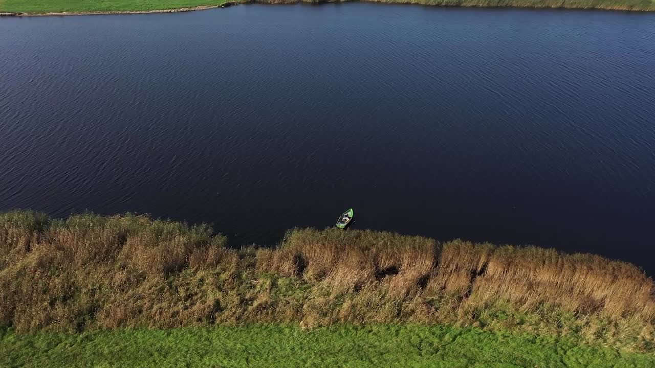 Drone's Aerial Sweep: Capturing a River Scene, A Fishing Boat, and a Fisher Amidst Rustling Reeds