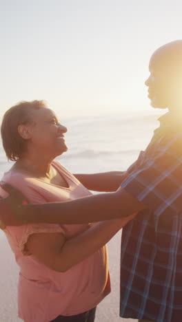 video vertical de una feliz pareja afroamericana de alto nivel abrazándose en una playa soleada