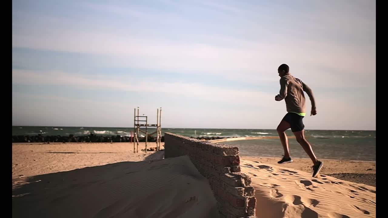 Corridore uomo afroamericano che fa jogging sulla spiaggia sotto il sole 4K