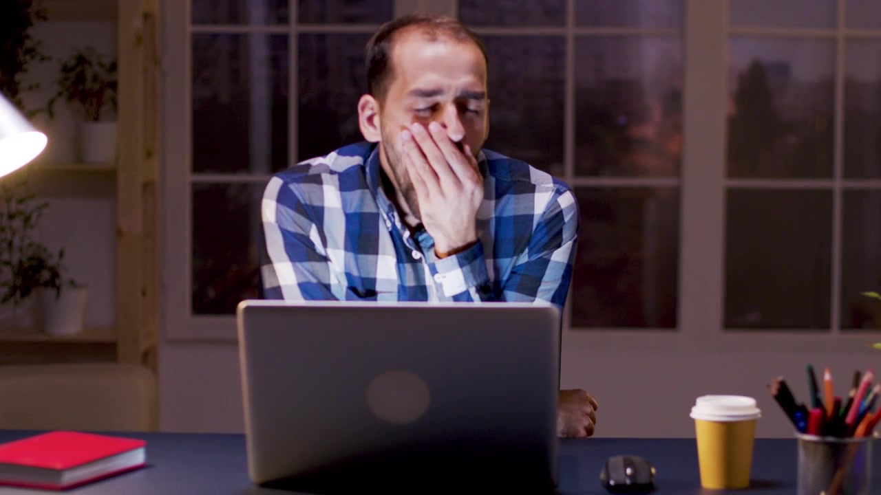 Tired Man Yawning While Working Late on Laptop at Night