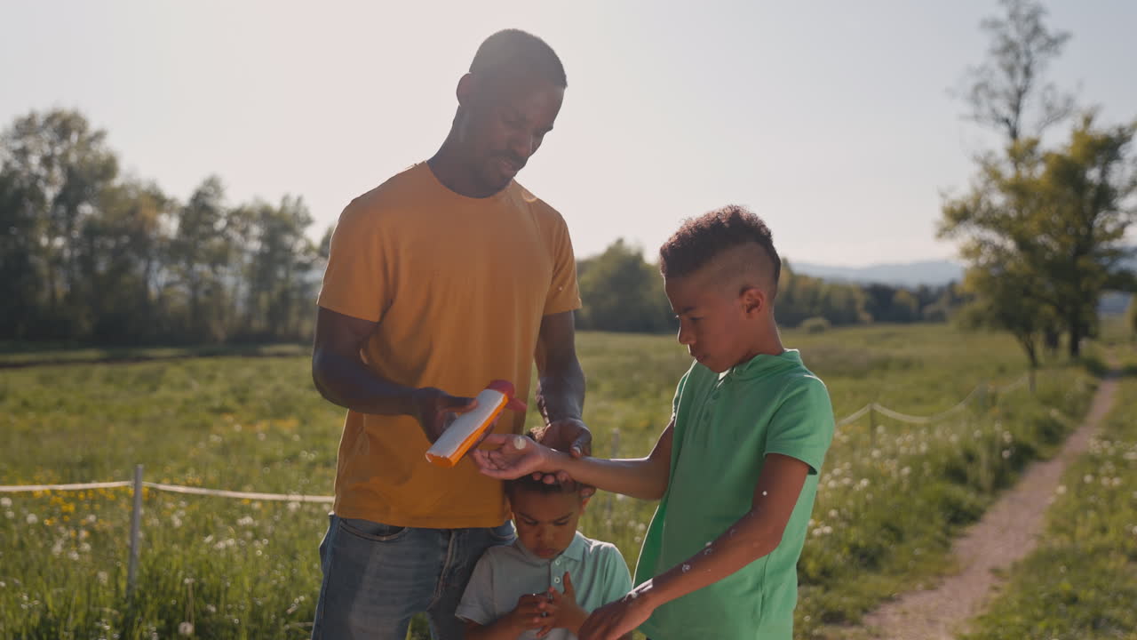 Un padre che mette la crema solare sui suoi figli per proteggerli, mentre trascorrono del tempo all'aperto in estate