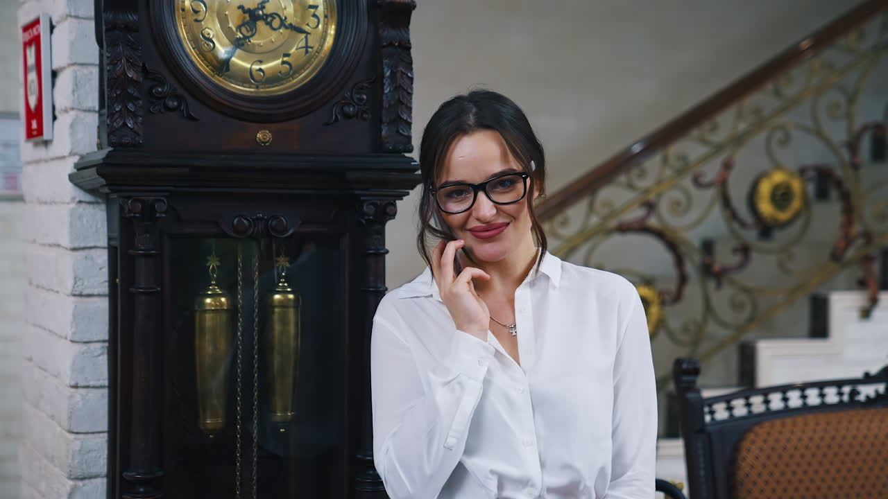 Portrait of business woman with a phone. Attractive girl in stylish glasses standing with a suitcase and talking the phone in the hotel.