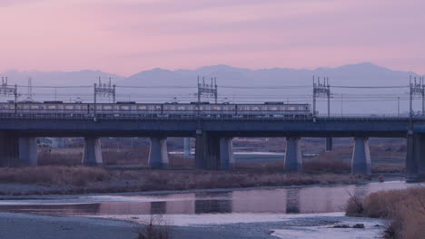 trains from futako-tamagawa station travelling across the bridge of tama river during sunset in tokyo, japan