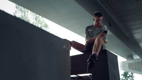 millennial relajado navegando por internet en línea en el teléfono móvil en el skatepark.