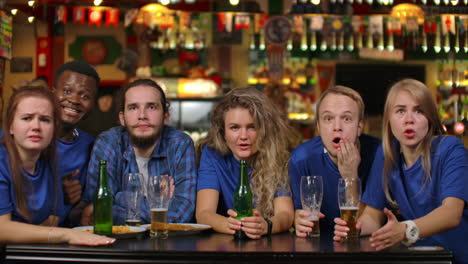 a group of young people watching the broadcast of a sporting event on tv in a beer bar emotionally waiting for a decisive moment and feeling sad after losing a team.