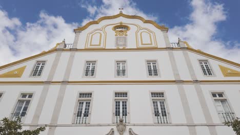 white facade of convento do colegio dos jesuitas with yellow ornaments under a blue sky with some clouds in portimao, portugal