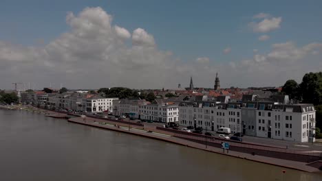 Enfoque-Aéreo-Del-Paisaje-Urbano-De-Zutphen,-Los-Países-Bajos,-Con-Tráfico-Que-Pasa-Por-El-Bulevar-Con-Fachadas-Blancas-Durante-El-Alto-Nivel-De-Agua-Del-Río-Ijssel-Que-Pasa-Por-Delante