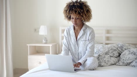 mujer joven que usa la computadora portátil en la cama