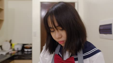 close-up shot of an asian black-haired schoolgirl in an apron preparing food in kitchen