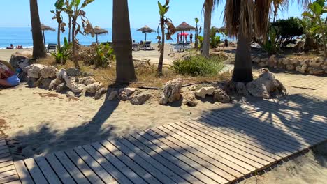 Walking-through-Spanish-beach-in-city-Estepona-with-palm-trees,-sand-and-sea-view,-Paseo-Maritimo