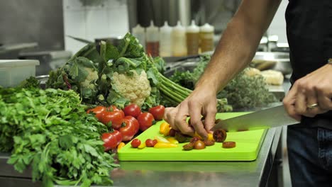 Chef-cutting-cherry-tomatoes-in-restaurant-kitchen-on-vegetable-background,-close-up