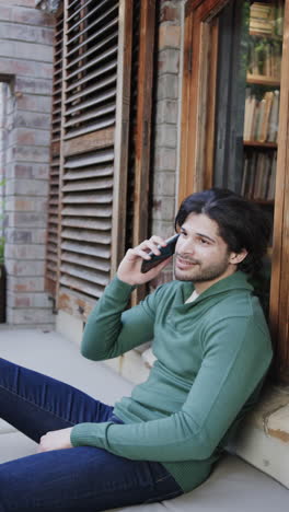 vertical video of happy biracial man talking on smartphone in window, slow motion