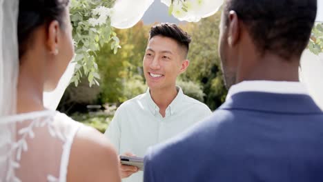 biracial man officiating marriage of happy african american couple in sunny garden, in slow motion