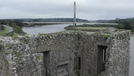 rising aerial of castle ruin reveals modern cable-stayed bridge beyond