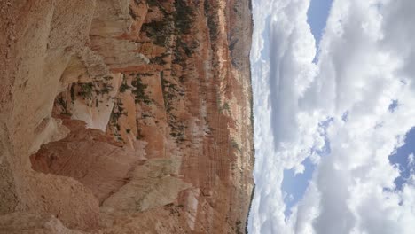 Tilt-up-vertical-shot-revealing-a-large-valley-of-orange-sandstone-hoodoo-formations-surrounded-by-greenery-and-trees-in-the-desert-of-Southern-Utah-on-a-warm-sunny-summer-day