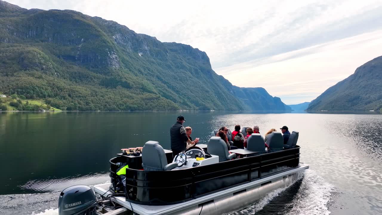 Drone closely follows Pontoon boat in remote Veafjord, tourists enjoying stunning mountain views