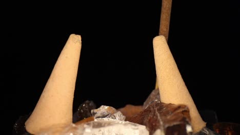 pasando varios conos de incienso apagados en un jardín de rocas decorativas, alejándose de un palo que ya no humea