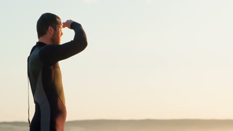 Vista-Lateral-De-Un-Surfista-Caucásico-De-Mediana-Edad-Con-Ojos-Protectores-Mirando-El-Mar-En-La-Playa-4k