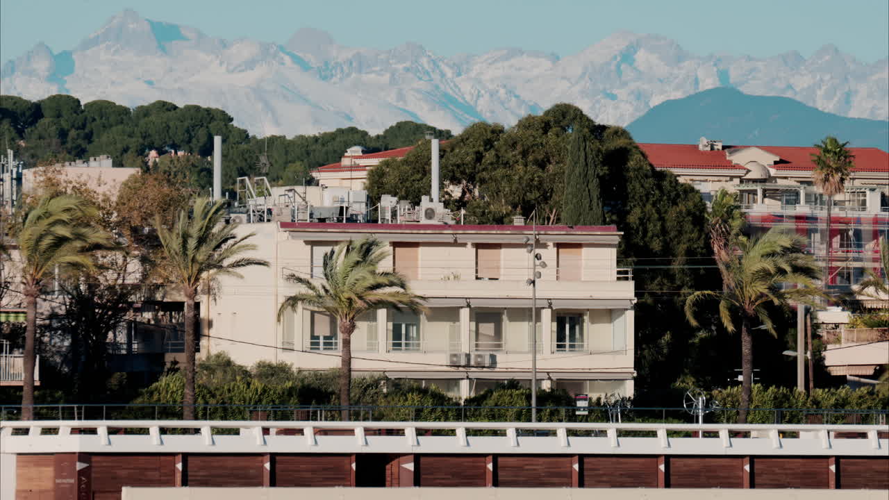 Buildings and palm trees on the shore with a view of the mountains in the background in Antibes, France