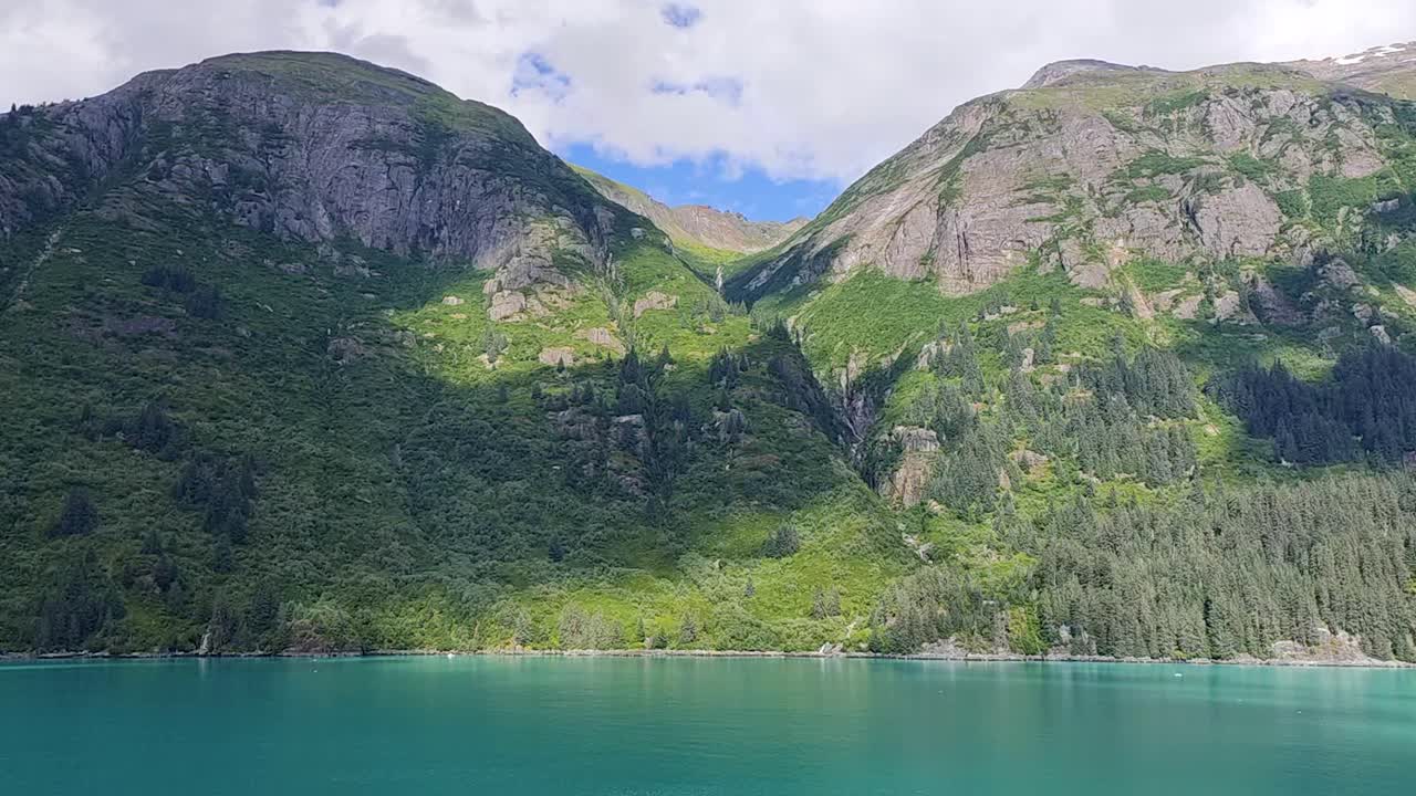 Fiordo panoramico con montagne verdi lussureggianti e acqua turchese.