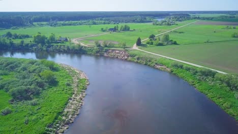 aerial view of a venta river on a sunny summer day, lush green trees and meadows, beautiful rural landscape, wide angle drone dolly shot moving left