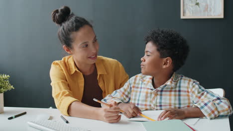 african boy doing homework at home with help of mother