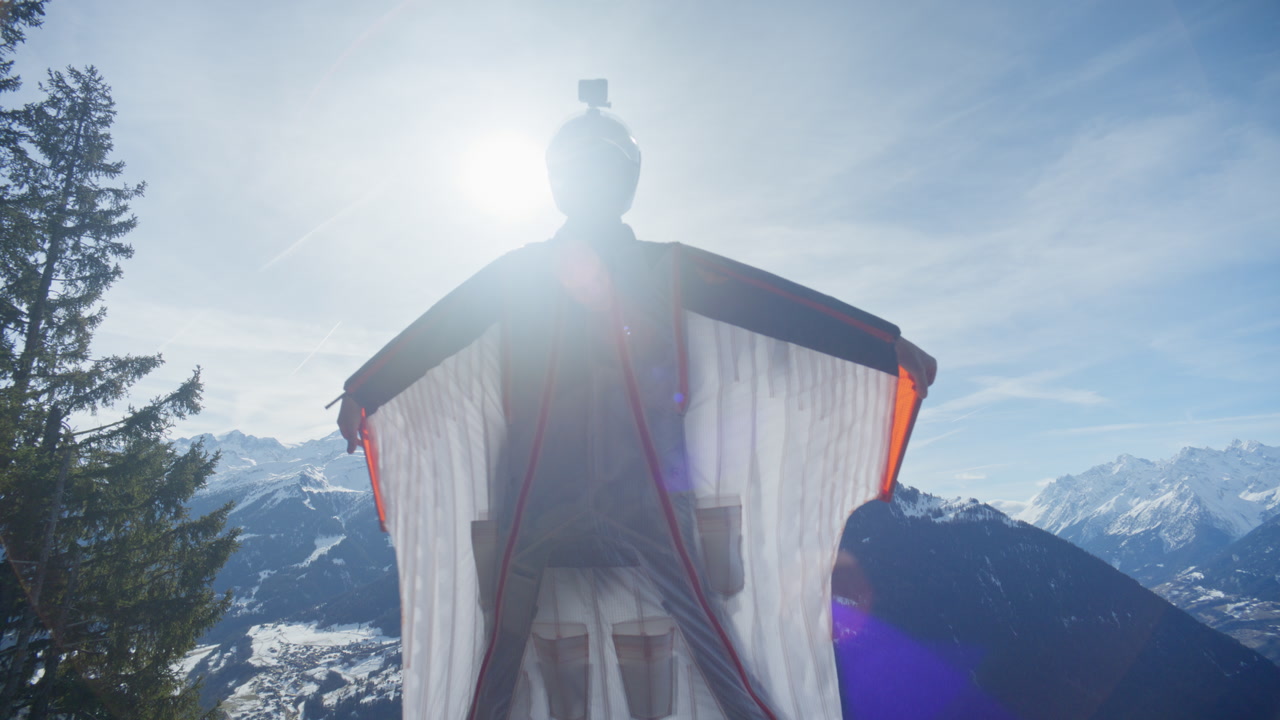 Wingsuit BASE jumper flying over Verbier surrounded by alpine mountains with snow-covered peaks. High-speed flight, dramatic scenery, and cinematic extreme sports action in the Swiss Alps.