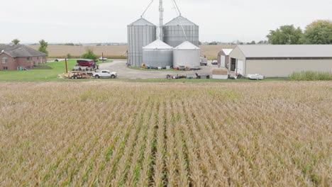 aerial flyover of cornfield with grain silos and farm machinery in the distance