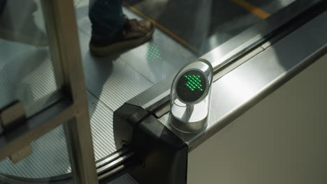 close-up shot capturing the lower part of people wearing black boots going down an escalator. the focus is on the mechanical parts of the escalator and the green directional light