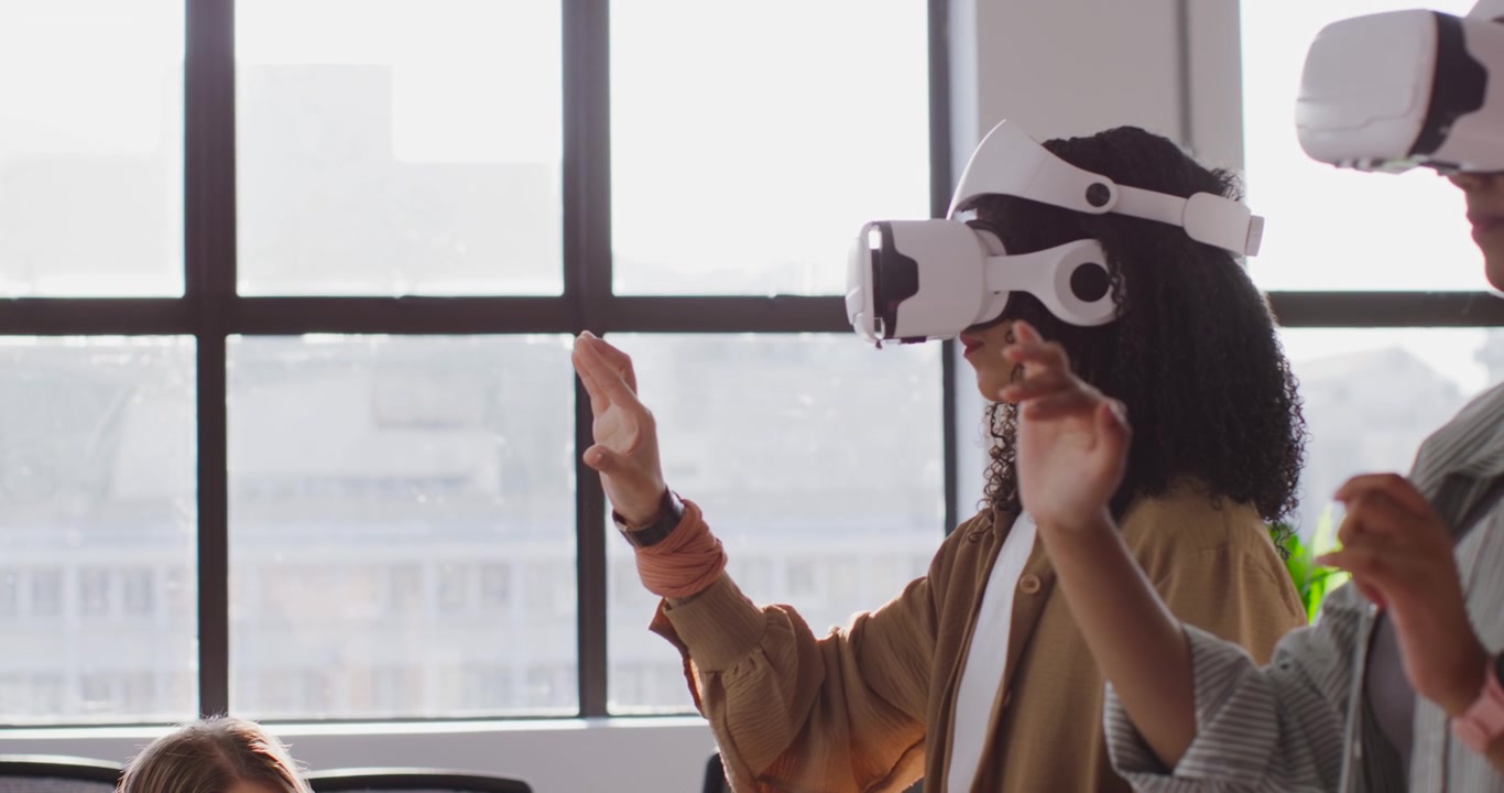 Team femminile che testa la realtà virtuale al lavoro dopo che una collega che gesticola e tiene in mano un tablet osserva i visori