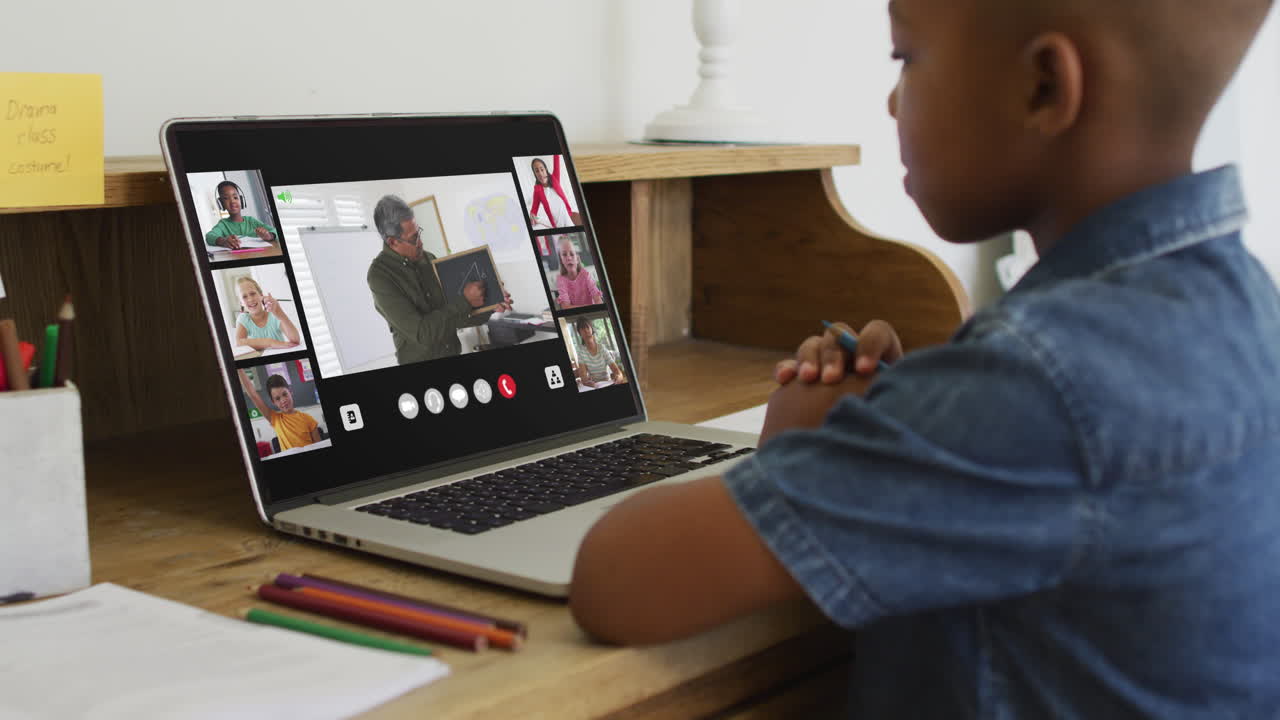African american boy holding a pencil having a video conference on laptop at home