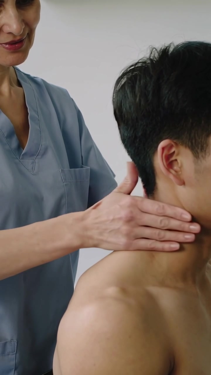 Video verticale: Terapista in divisa blu che posiziona le mani e preme lungo il lato destro del collo del cliente in clinica