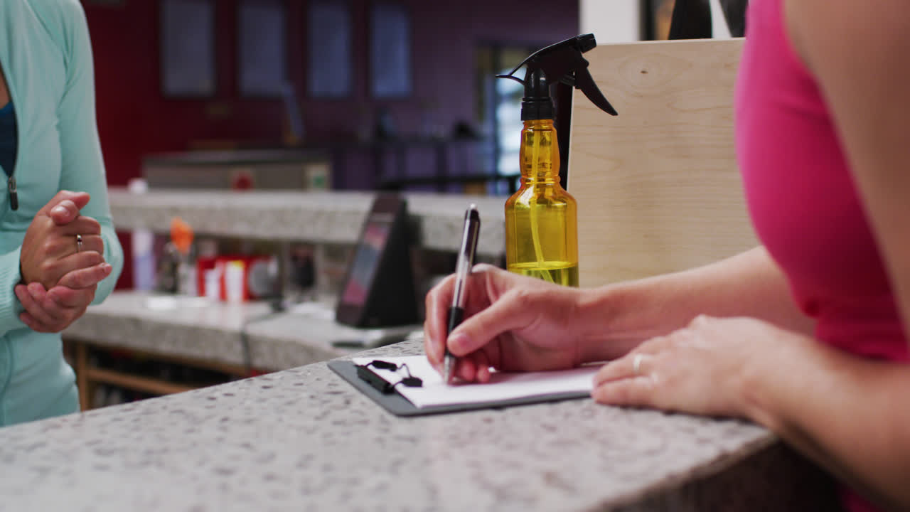 체육관 리셉션의 카운터에서 양식을 채우는 백인 여성의 중간 섹션