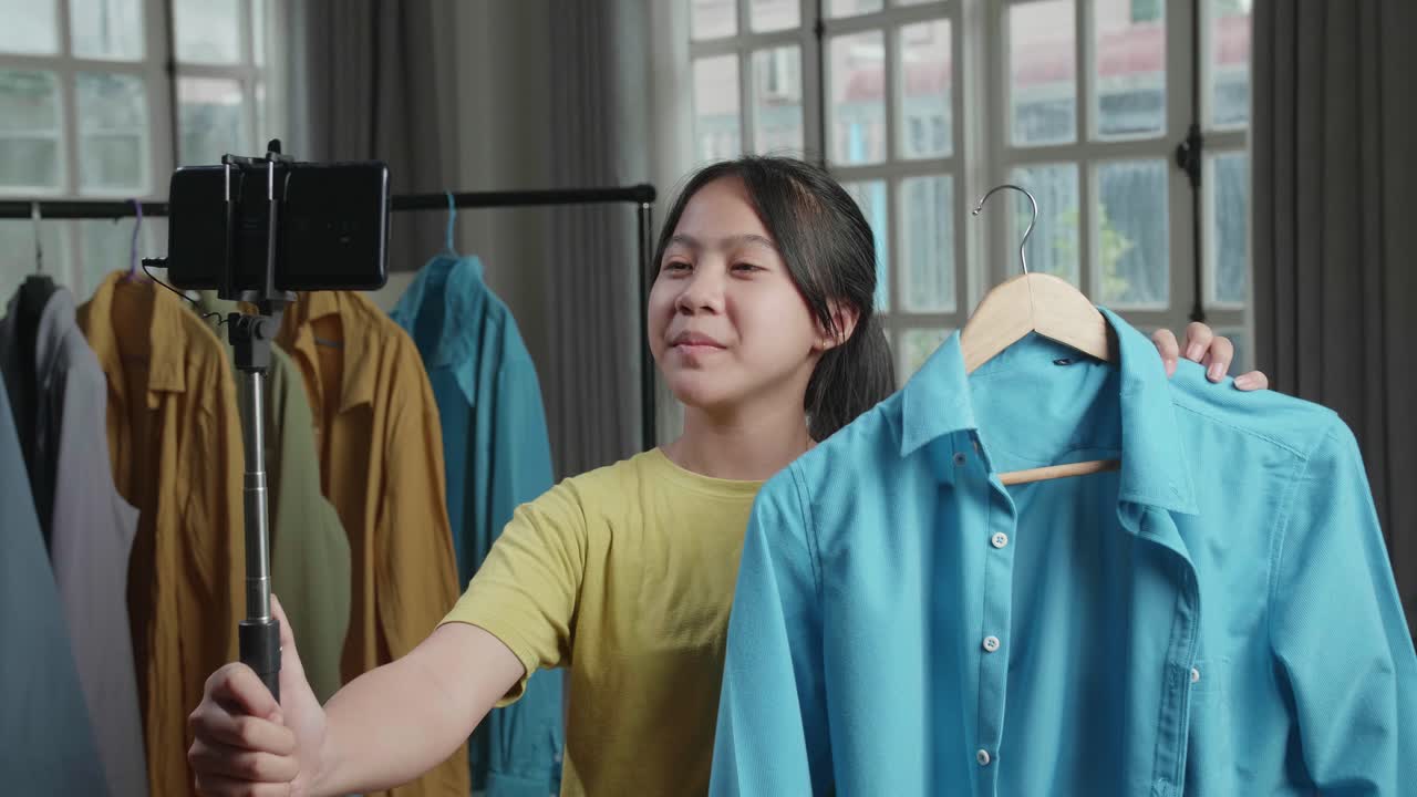 Asian Young Girl Online Seller Recommending A Shirt And Recording Video By Mobile Phone While Selling Clothes At Home