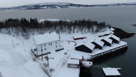 vista de avión no tripulado en el área de tromsø volando sobre finnsnes en invierno y mostrando el mar al lado de la ciudad nevada dando vueltas alrededor de un hotel en noruega