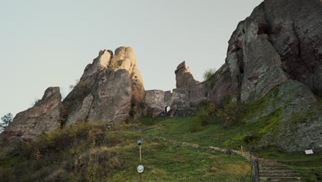 Reveal-shot-of-the-historic-Belogradchik-rock-formation-in-Bulgaria,-including-stone-steps-and-green-grass-along-the-hillside