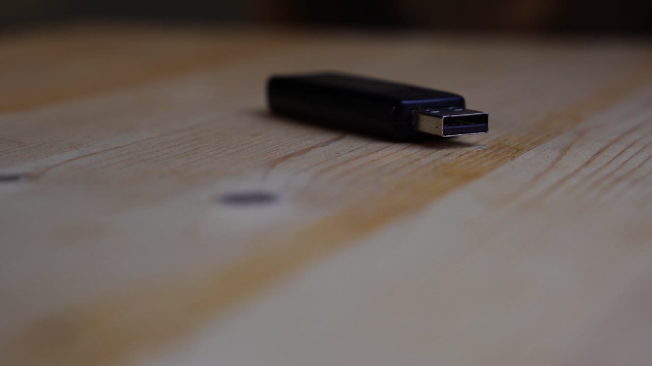 la memoria usb negra se encuentra sobre una tabla de madera y gira sobre un fondo oscuro