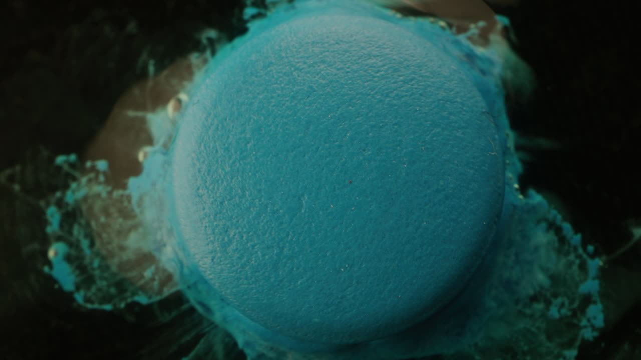 Close-up of a blue round object with a textured surface, possibly a macaron or painted object, after an explosion of liquid or paint