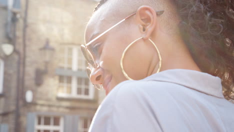 fashionable young black woman wearing sunglasses talking on the street, close up, side view, lens flare