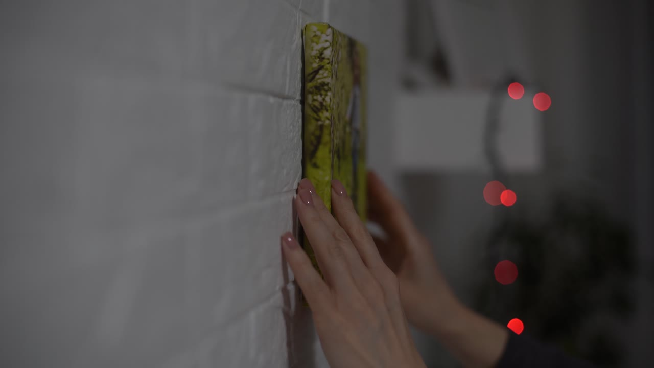 한 여성이 벽에 사진 캔버스를 매달고 있다.